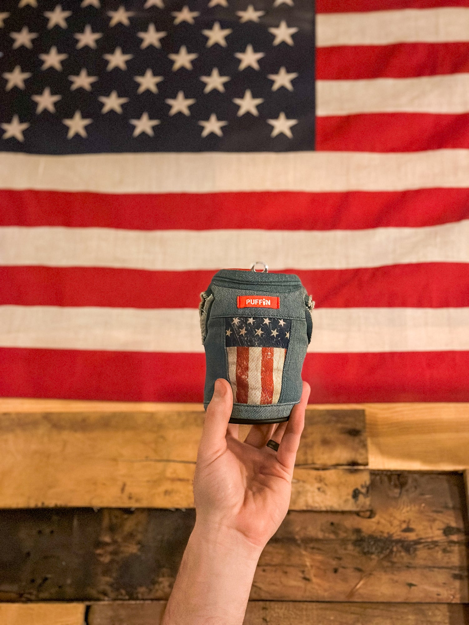 The Denim Vest Merica being held up in front of an American Flag.